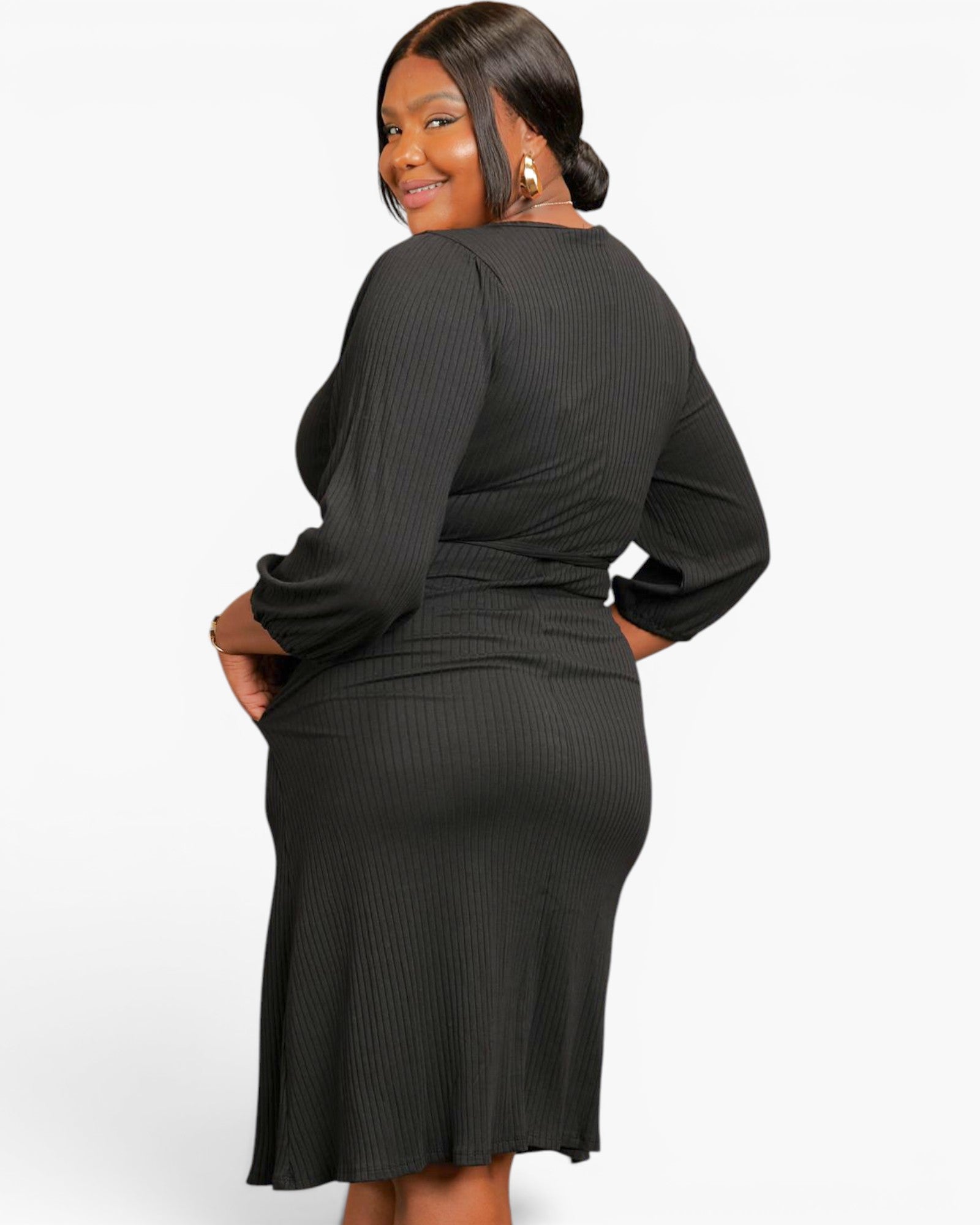 A woman modeling a dark charcoal ribbed long-sleeve midi dress, shown from a three-quarter back angle against a plain white studio background.