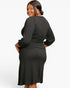 A woman modeling a dark charcoal ribbed long-sleeve midi dress, shown from a three-quarter back angle against a plain white studio background.