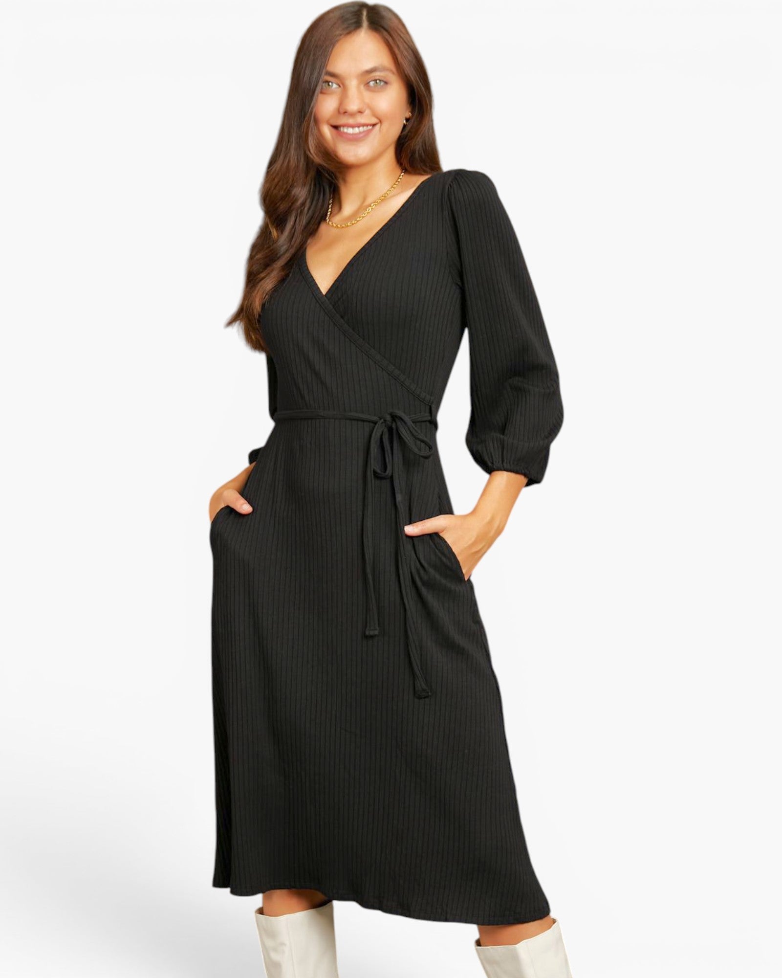 A woman modeling a black ribbed midi wrap dress with three-quarter puff sleeves, side pockets, and a self-tie waist belt, paired with white boots against a plain white studio background.