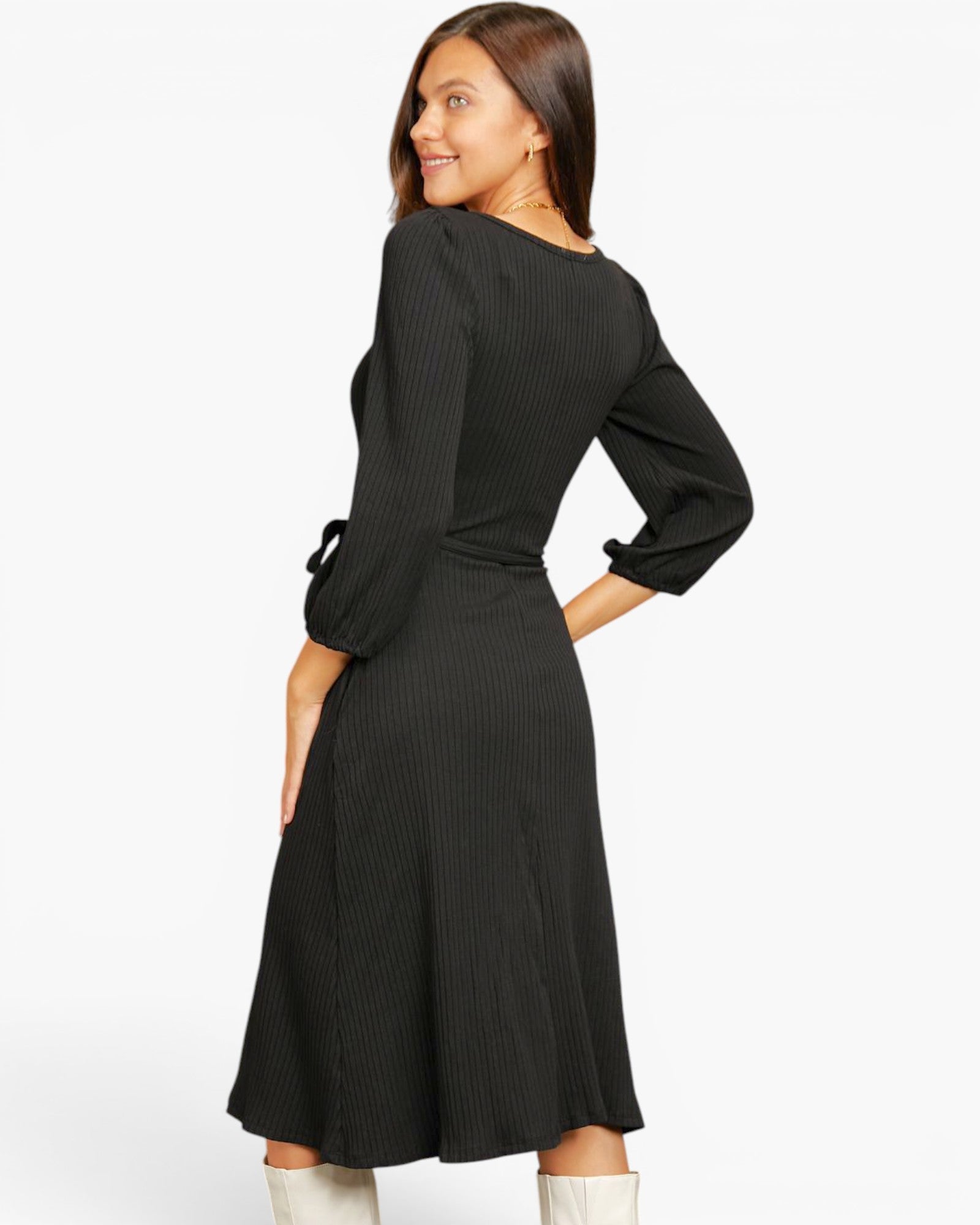 A woman modeling a black ribbed long-sleeve midi dress with a tie detail on the cuffs, shown from a three-quarter back angle against a plain white studio background.