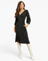 A woman modeling a black ribbed wrap midi dress with three-quarter sleeves, a tie waist, and side pockets, paired with off-white knee-high boots against a light gray studio background.
