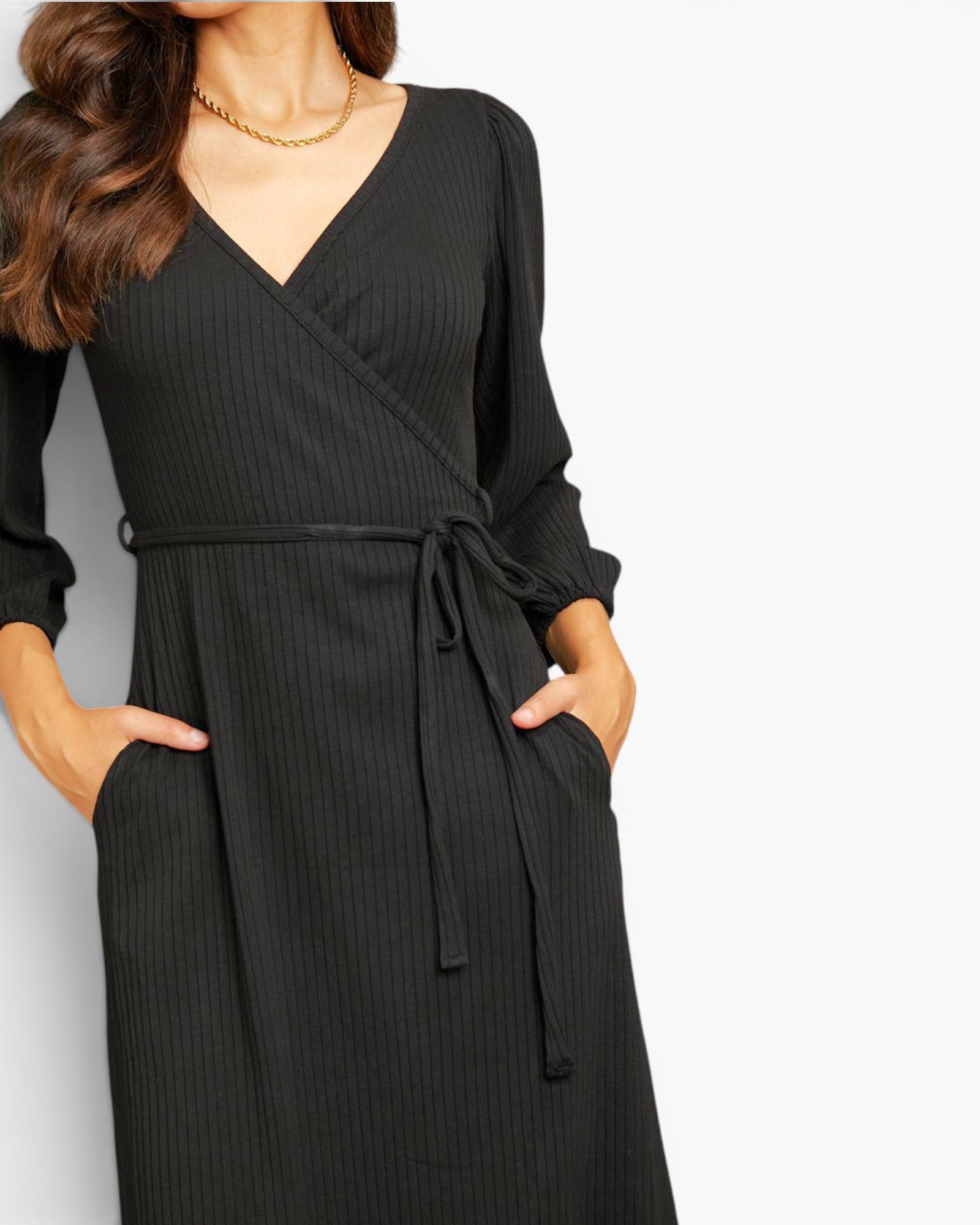 A woman wearing a black ribbed long-sleeve wrap dress with a tie waist and side pockets, shown against a plain light background.