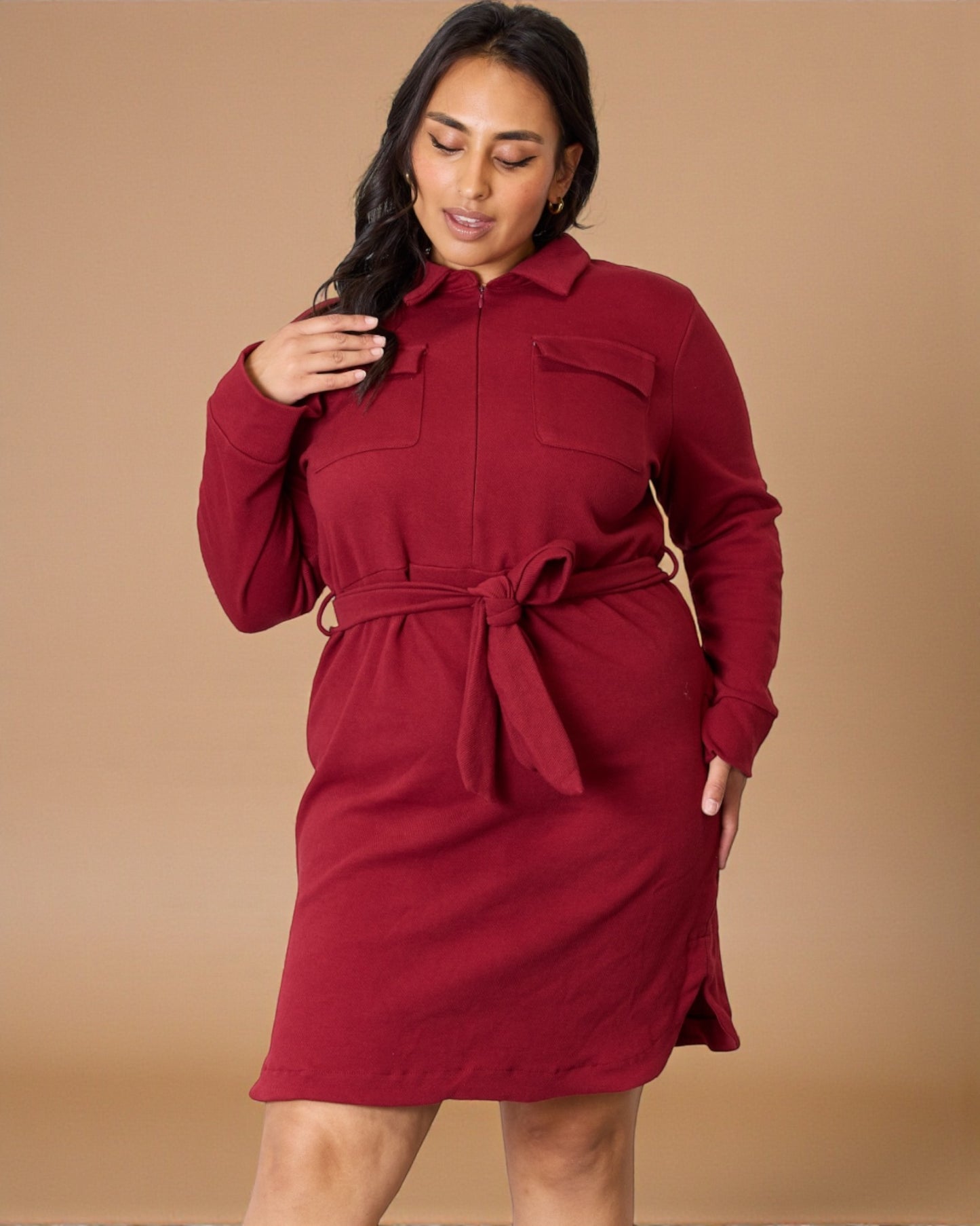 Woman wearing a red dress with a belt against a beige background