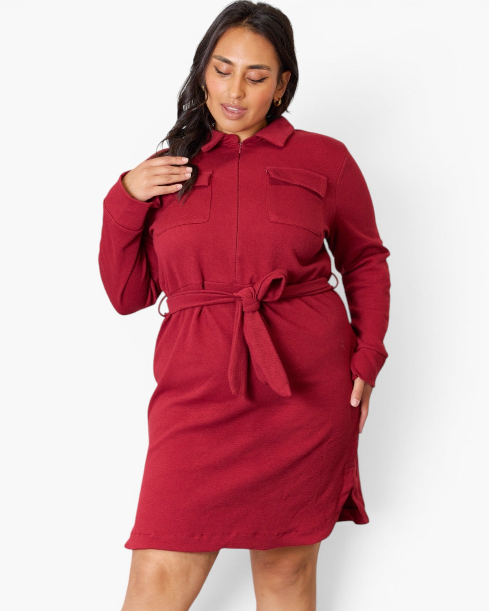 A woman modeling a long-sleeve red collared shirt dress with a matching tie belt, shown against a plain light gray studio background.