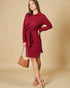 Woman wearing a red dress with a belt, holding a brown handbag against a beige background