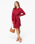 A woman modeling a long-sleeve red collared shirt dress with a matching tie belt, holding a small brown handbag against a plain light gray studio background.