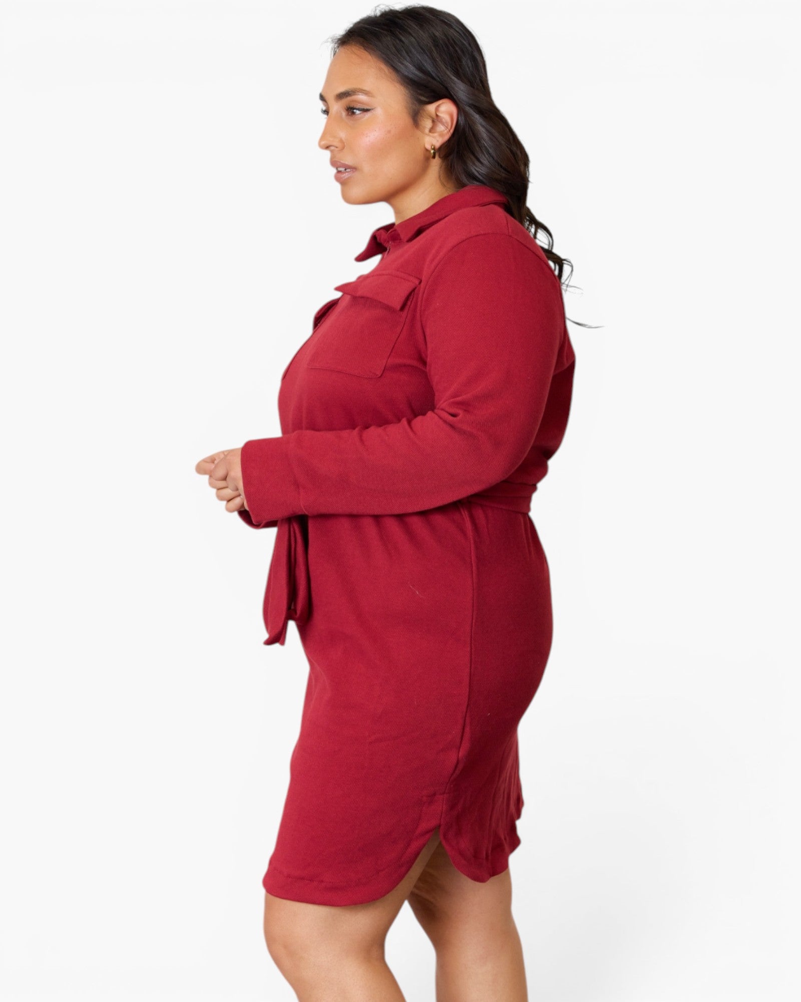 A woman wearing a long-sleeve red shirt dress, shown from a side profile against a plain white studio background.