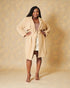 Woman wearing a beige trench coat against a gold background