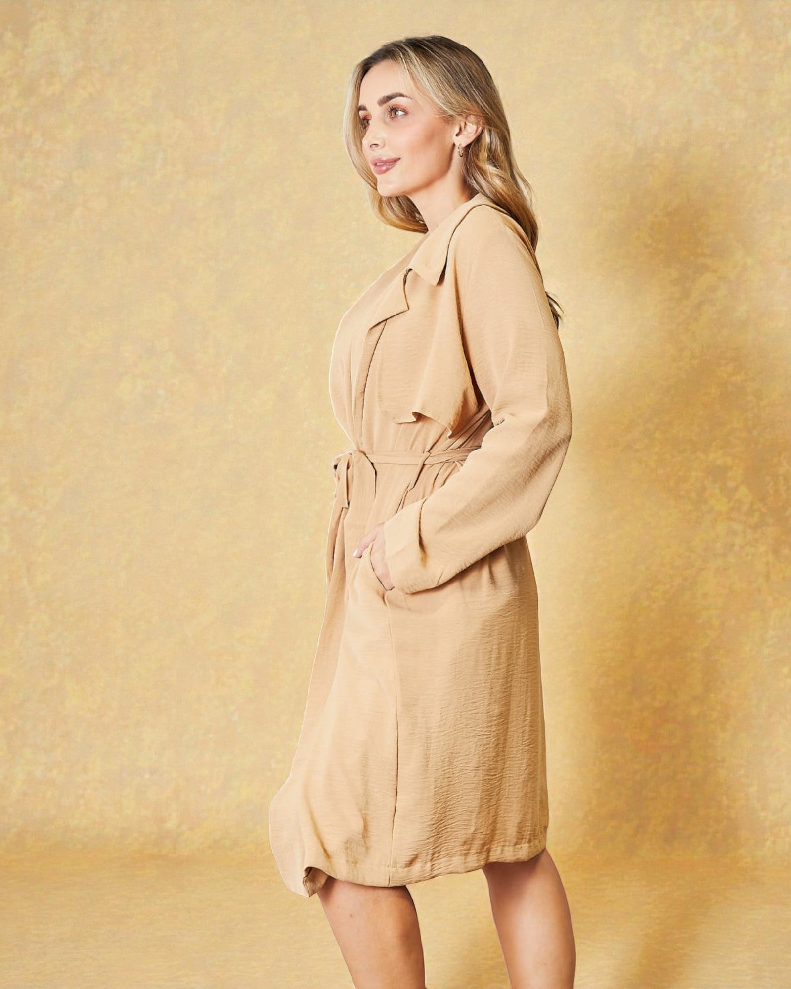 Woman wearing a beige trench coat against a yellow background