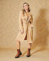 Woman wearing a beige trench coat and brown boots against a beige background