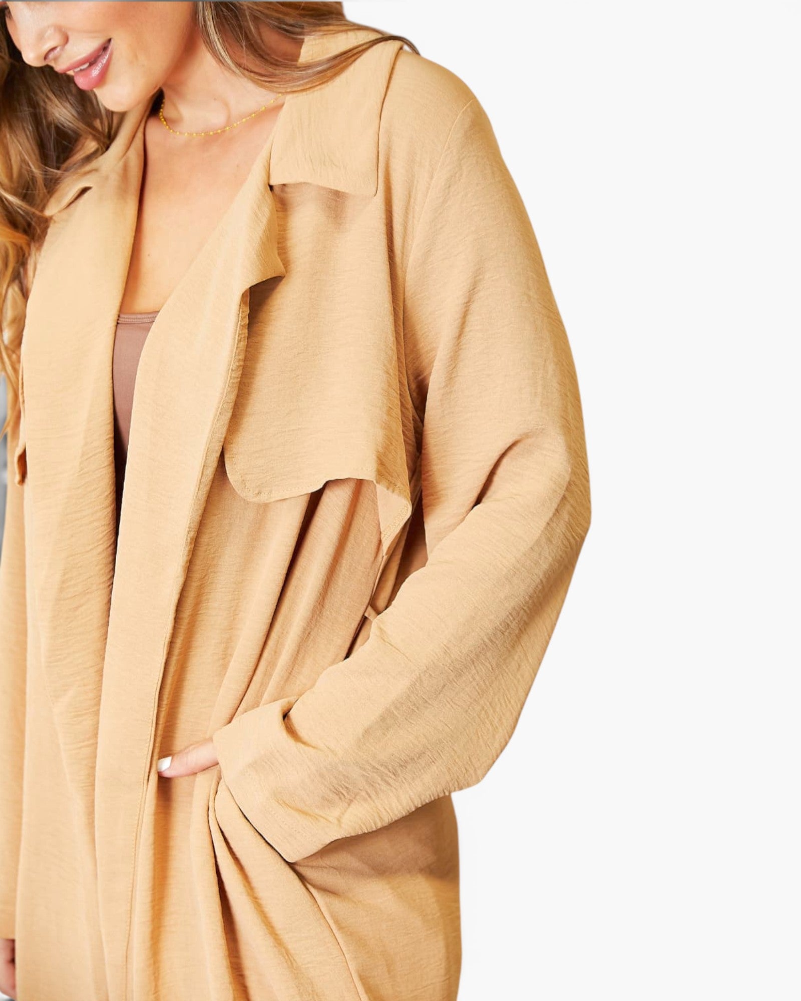 A close-up of a woman wearing a loose, long-sleeve tan jacket or overshirt over a mauve top, shown against a plain light background.