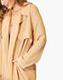A close-up of a woman wearing a loose, long-sleeve tan jacket or overshirt over a mauve top, shown against a plain light background.
