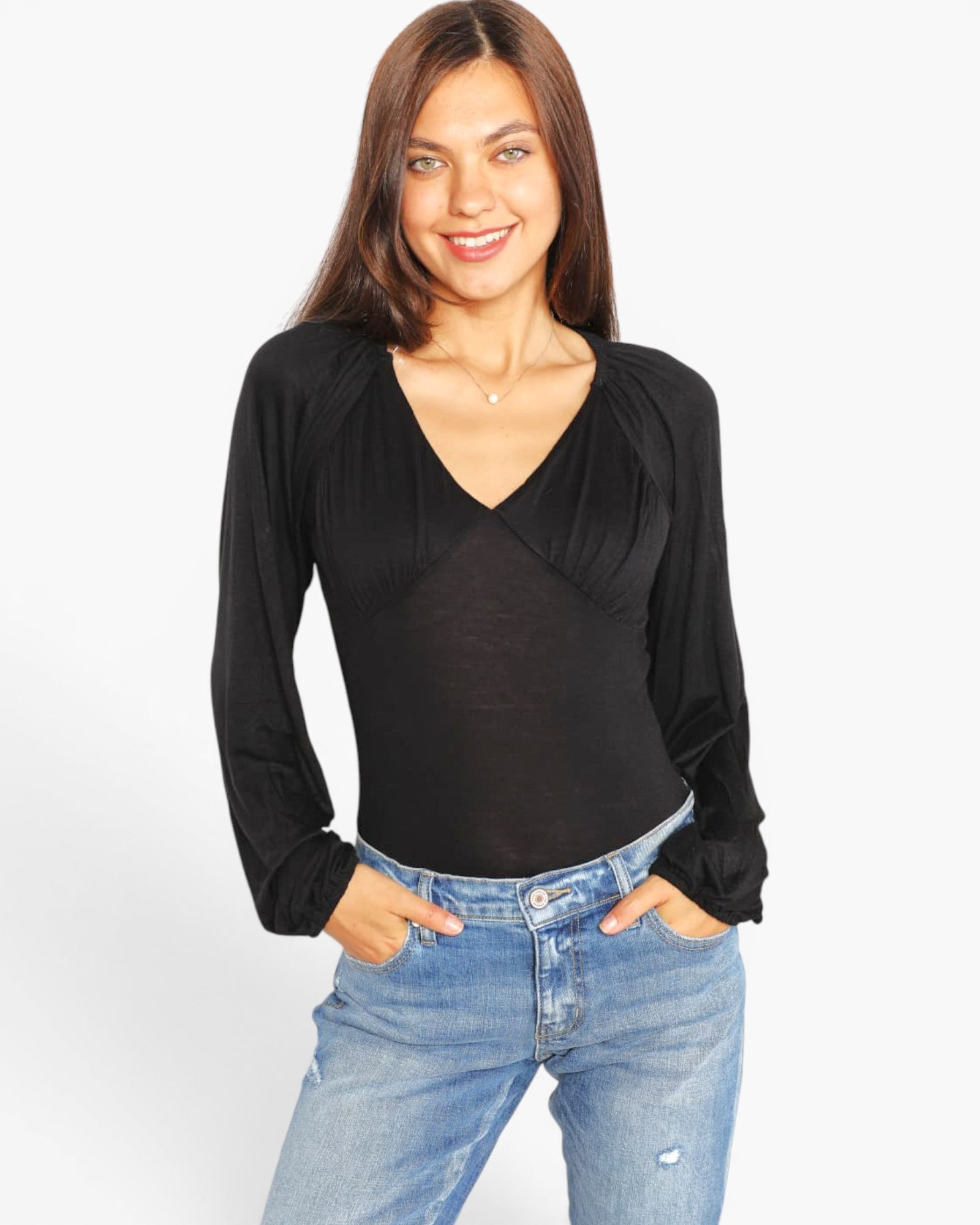 A woman modeling a black long-sleeve top with a draped V-neckline, paired with blue jeans, against a plain white studio background.