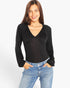 A woman modeling a black long-sleeve top with a draped V-neckline, paired with blue jeans, against a plain white studio background.