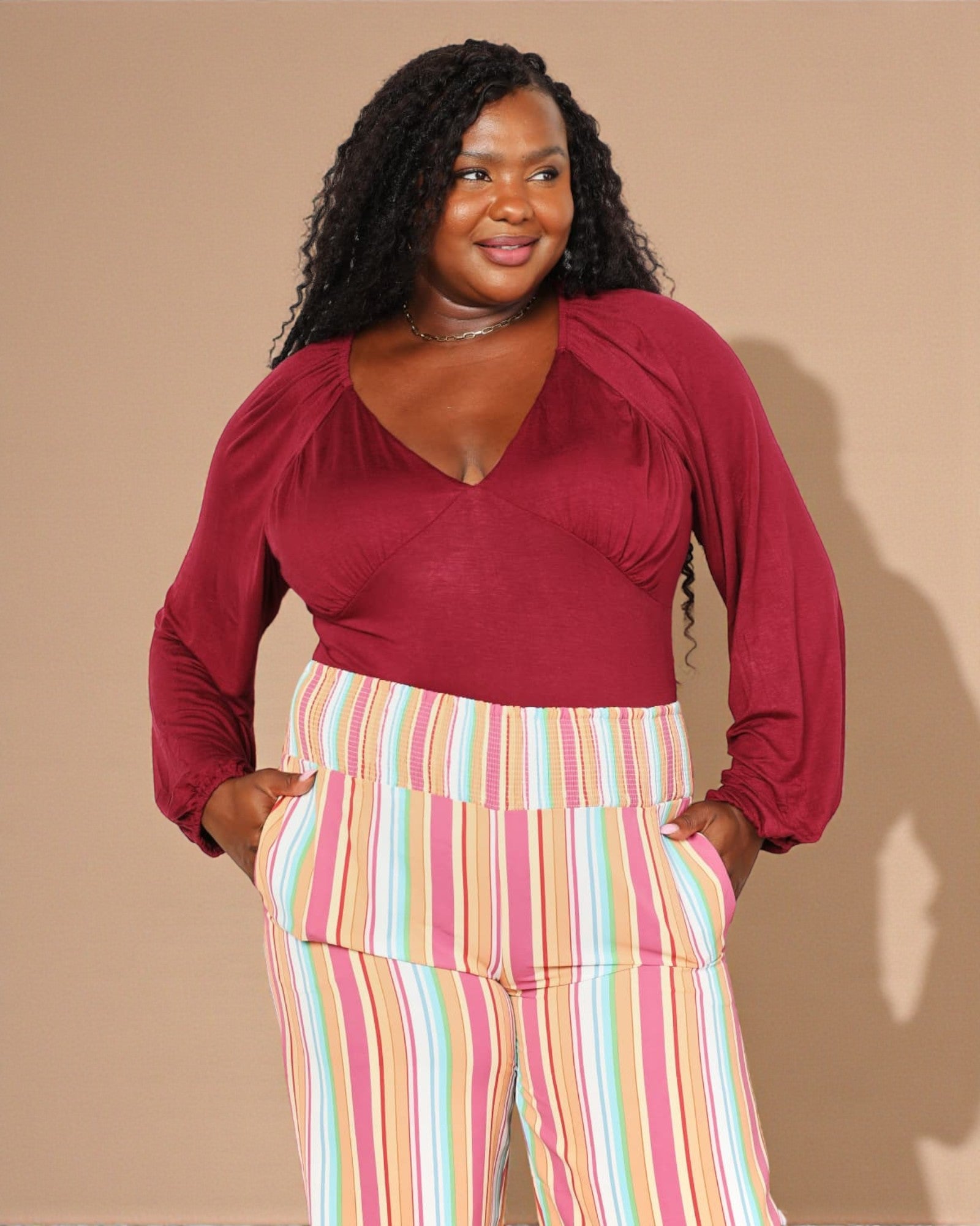 Woman wearing a red top and colorful striped pants against a beige background