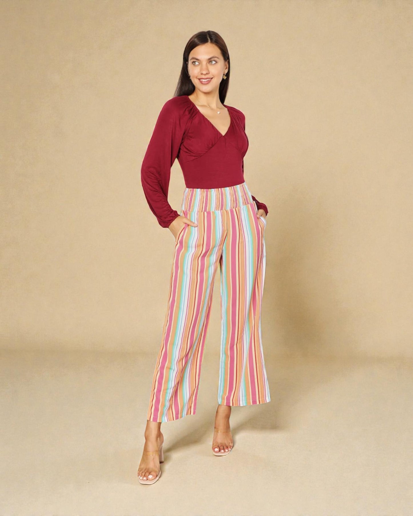 Woman wearing a red top and colorful striped pants on a beige background