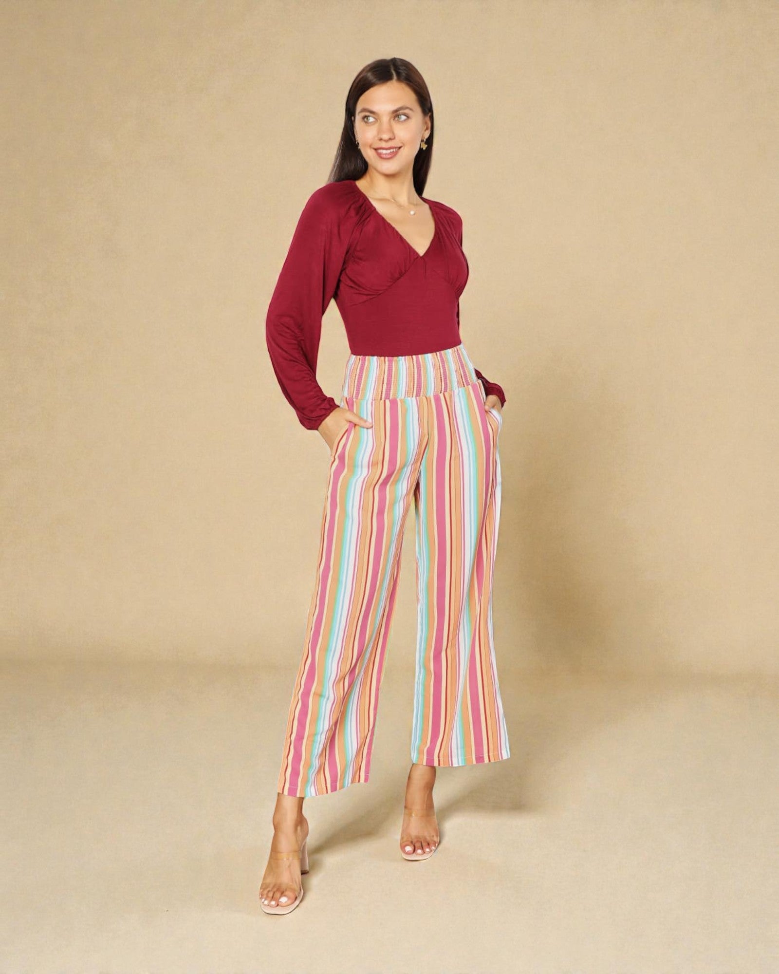 Woman wearing a red top and colorful striped pants on a beige background