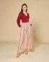 Woman wearing a red top and colorful striped pants on a beige background