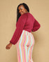 Woman wearing a red top and colorful striped pants against a beige background
