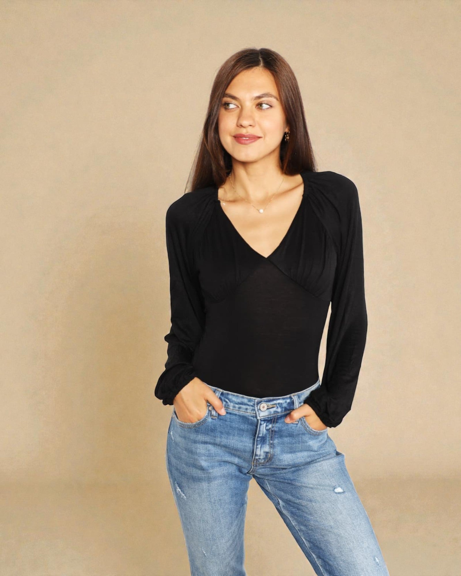Woman wearing a black long-sleeve top and blue jeans against a beige background
