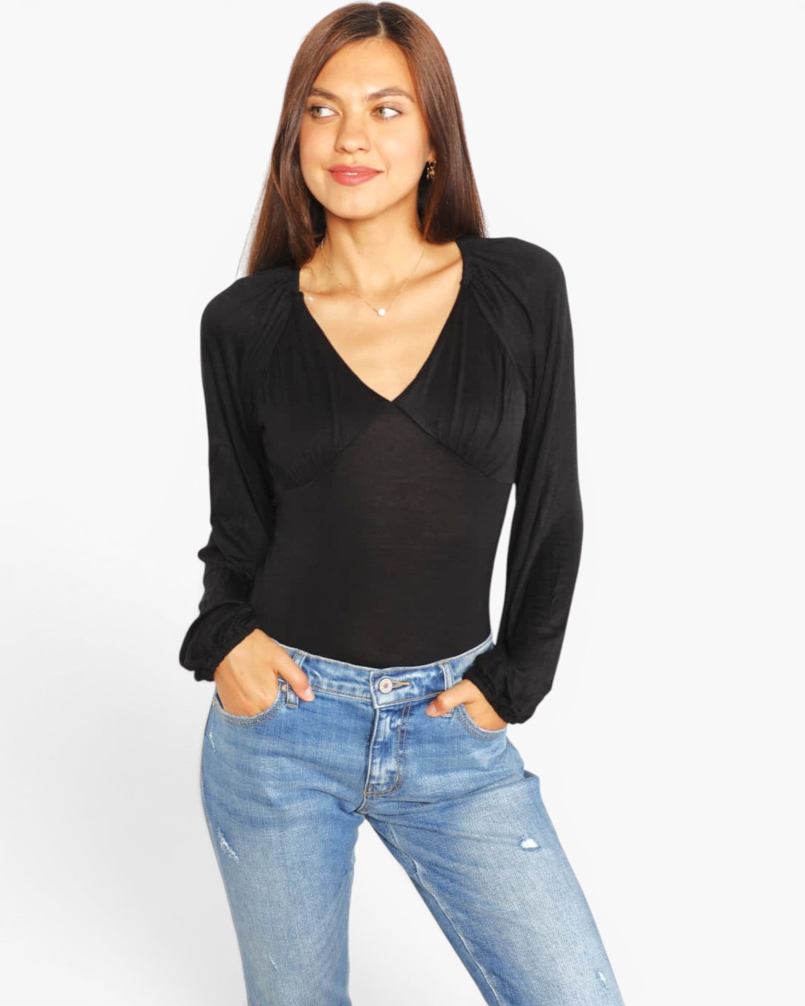 A woman modeling a black long-sleeve top with a V-neck and gathered shoulders, paired with light blue jeans, against a plain white background.