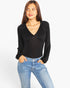 A woman modeling a black long-sleeve top with a V-neck and gathered shoulders, paired with light blue jeans, against a plain white background.