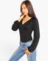 A woman modeling a black long-sleeve top with a deep V-neck and voluminous balloon sleeves, paired with blue jeans, against a plain white background.