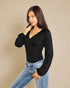 Woman wearing a black long-sleeve top and blue jeans against a beige background