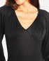 A close-up of a woman wearing a black long-sleeve top with a deep V-neck and gathered draping details on the chest and shoulders.