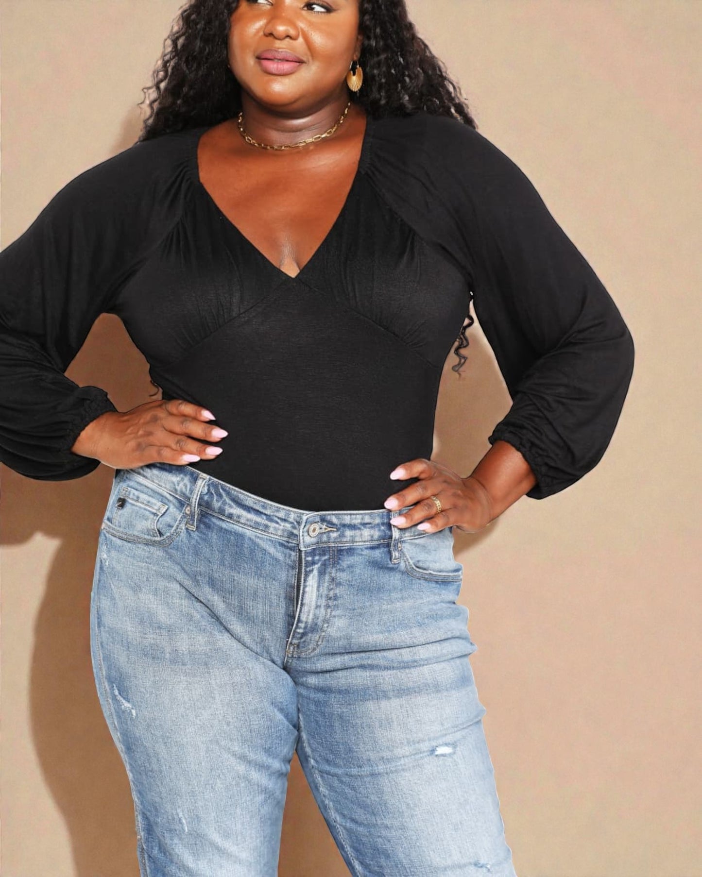 Person wearing a black long-sleeve top and blue jeans against a beige background