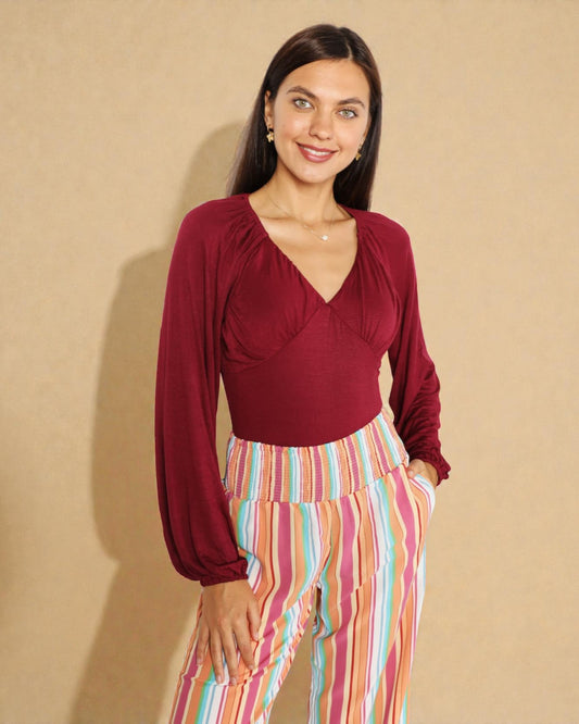Woman wearing a burgundy top and colorful striped pants against a beige background