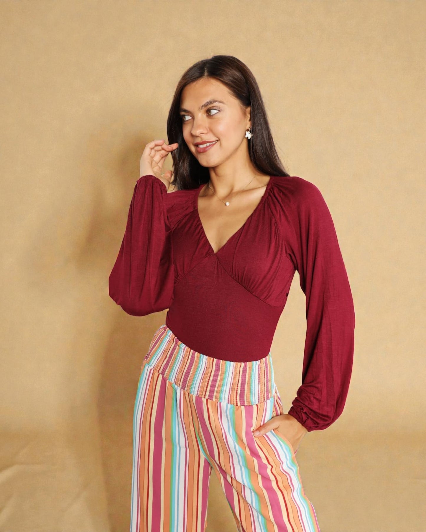 Woman wearing a burgundy top and colorful striped pants against a beige background