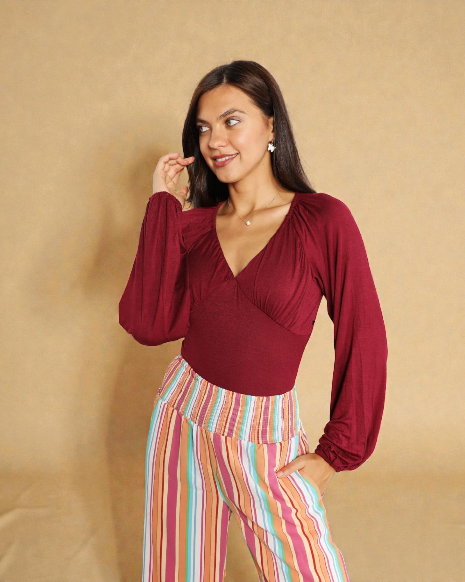 Woman wearing a burgundy top and colorful striped pants against a beige background