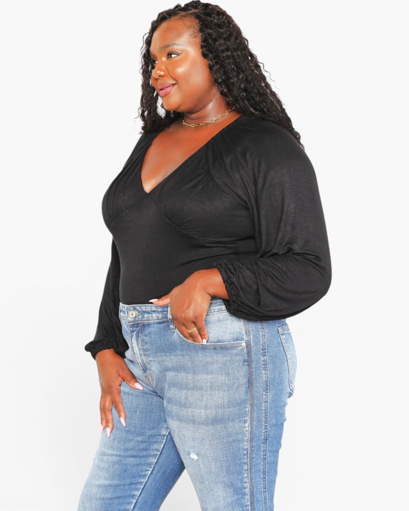 A woman modeling a black long-sleeve wrap-style top with gathered sleeves, paired with light blue jeans, against a plain white studio background.
