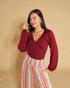 Woman wearing a burgundy top and colorful striped pants against a beige background