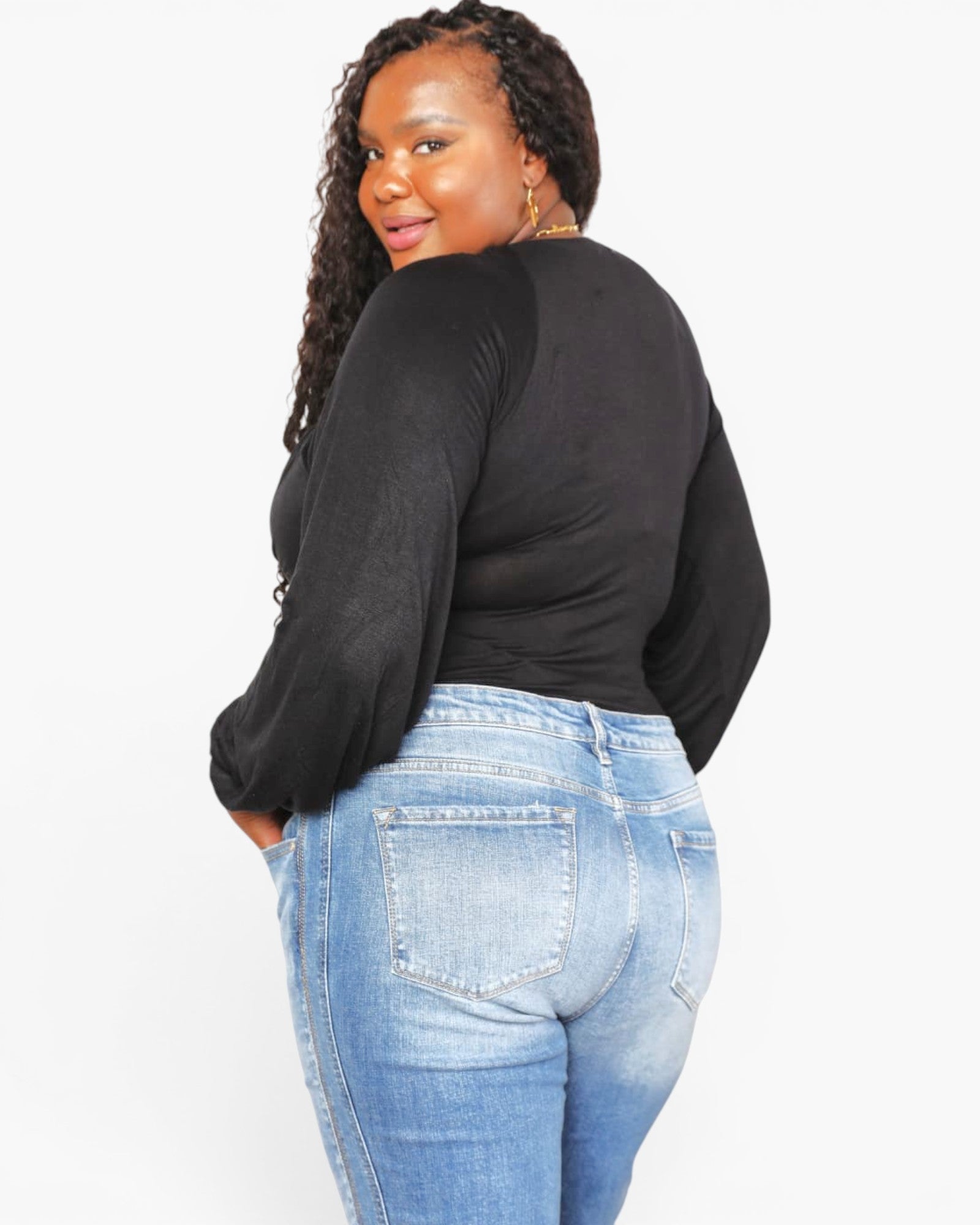 A woman wearing a black long-sleeve ribbed top and light blue jeans, photographed from the back against a plain white studio background.