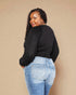 Woman wearing a black long-sleeve top and blue jeans against a beige background