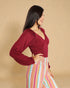 Woman wearing a burgundy long-sleeve top and colorful striped pants against a beige background