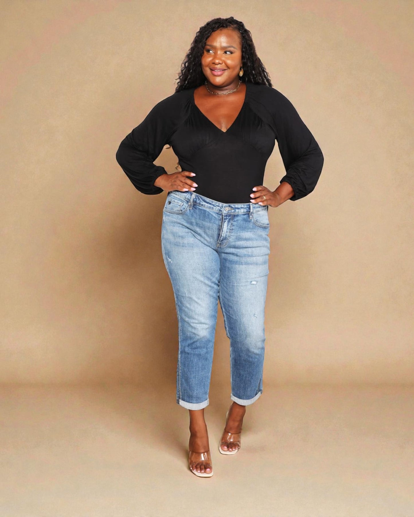 Woman wearing a black top and blue jeans against a beige background