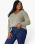 A woman modeling a sage green long-sleeve V-neck top with dark blue jeans against a plain white studio background.