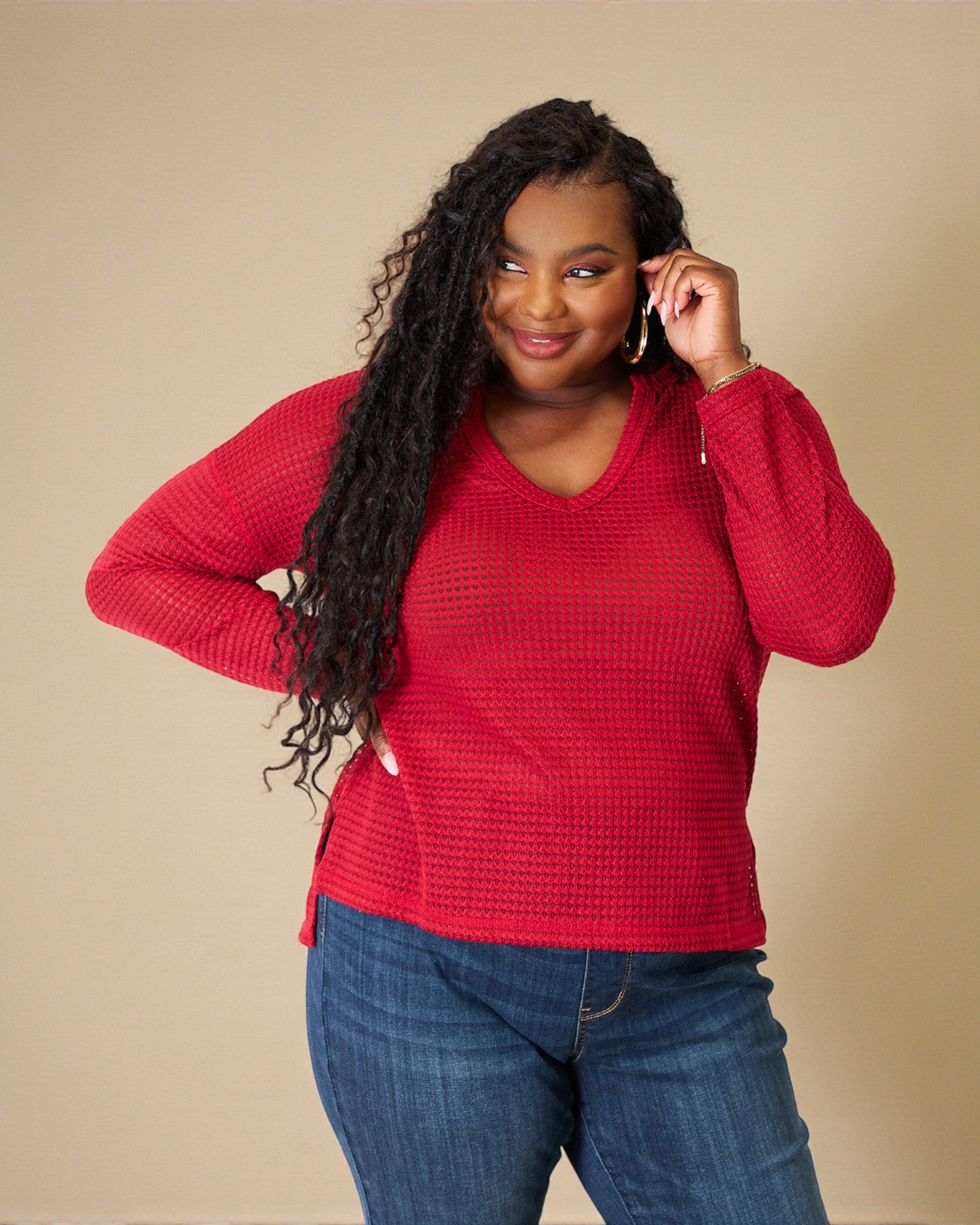 Woman wearing a red sweater and blue jeans against a beige background