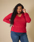 Woman wearing a red sweater and blue jeans against a beige background