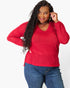 A woman wearing a bright red, long-sleeve waffle-knit V-neck top and blue jeans, posing against a plain white studio background.
