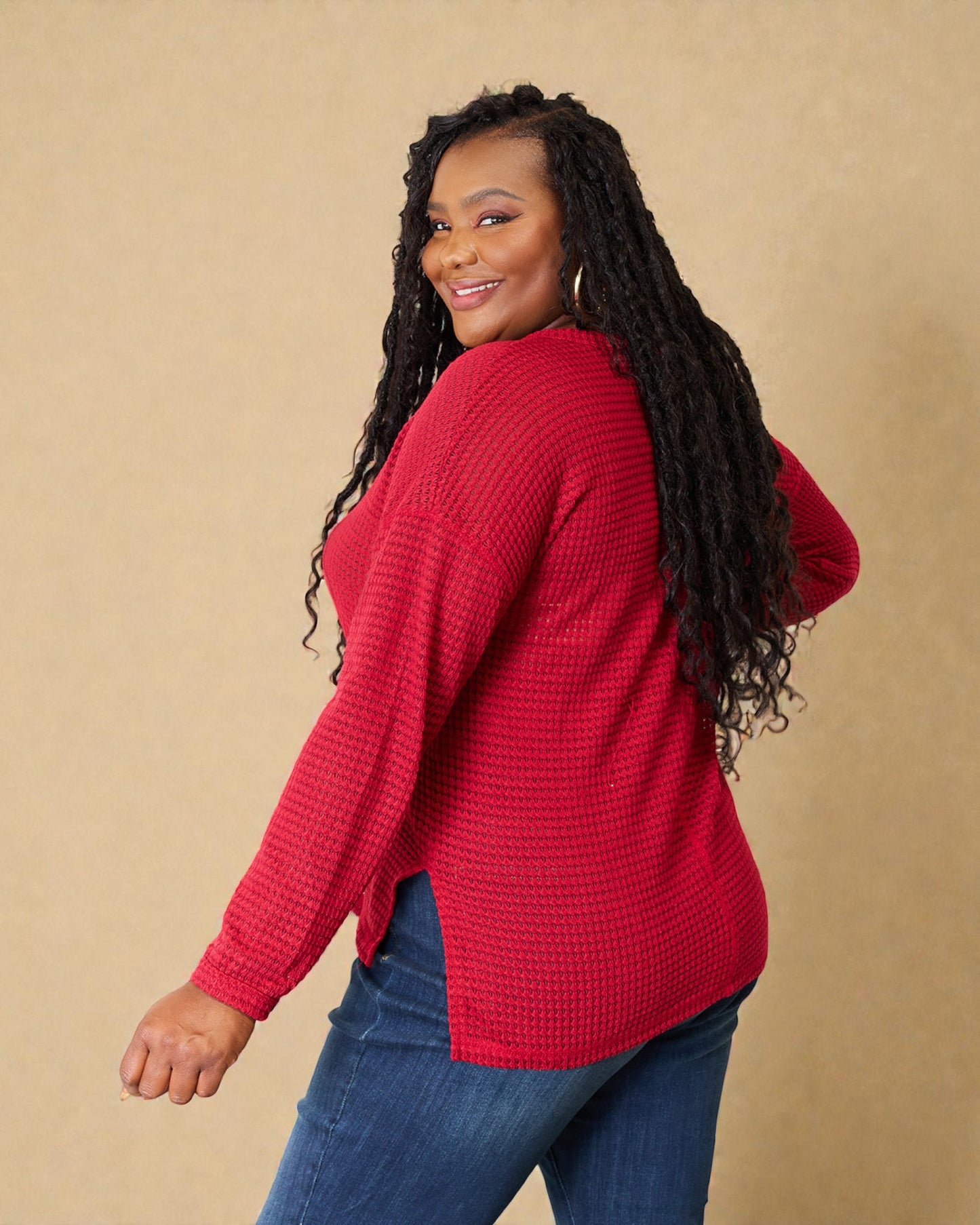 Woman wearing a red sweater and blue jeans against a beige background