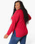 A woman with long black curly hair is shown from a three-quarters back view, wearing a bright red waffle-knit long-sleeve top and blue jeans against a plain white studio background.