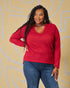 Woman wearing a red sweater and blue jeans against a beige background with white abstract patterns.