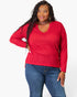 A woman modeling a bright red waffle-knit long-sleeve top with a V-neck, paired with blue jeans, against a plain white studio background.