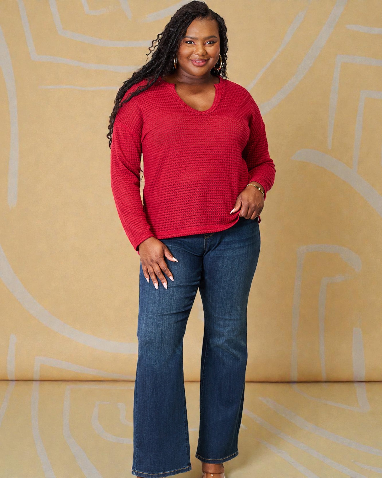 Woman wearing a red sweater and blue jeans against a beige background