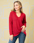 Woman wearing a red sweater and blue jeans against a beige background