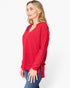 A woman wearing a red waffle-knit long-sleeve top with a split V-neckline, paired with blue jeans, photographed against a plain white studio background.